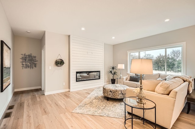 living area featuring baseboards, recessed lighting, light wood-style floors, and a fireplace