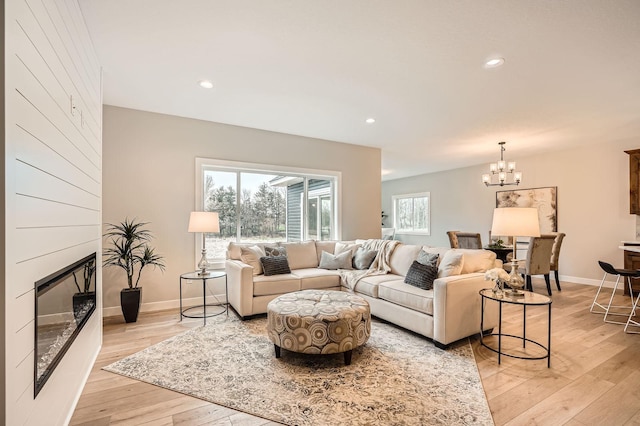 living area featuring a chandelier, baseboards, light wood-style flooring, and a fireplace
