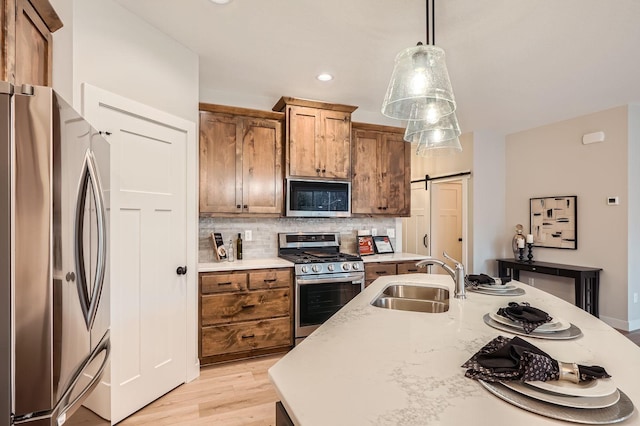 kitchen with a sink, stainless steel appliances, brown cabinetry, backsplash, and an island with sink