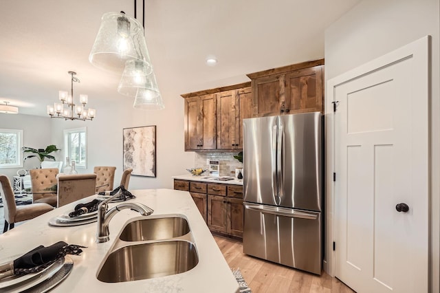 kitchen with light stone counters, decorative backsplash, freestanding refrigerator, light wood finished floors, and pendant lighting