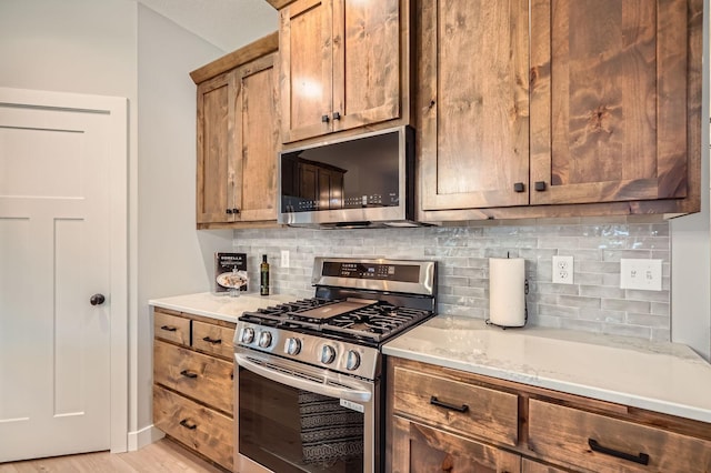 kitchen featuring tasteful backsplash, light stone counters, brown cabinetry, stainless steel appliances, and light wood finished floors