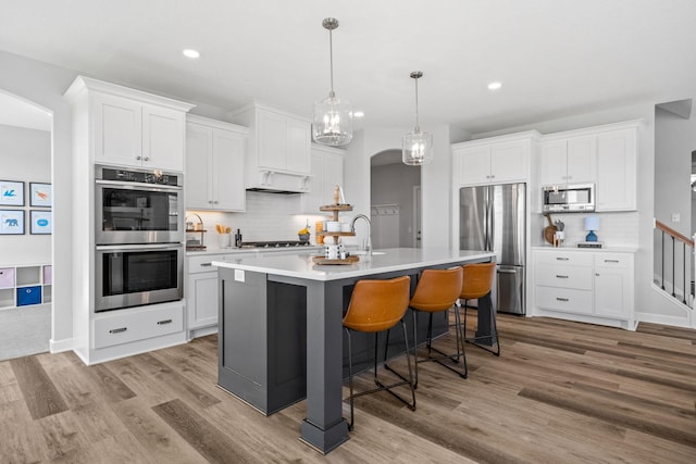 kitchen with arched walkways, a breakfast bar area, stainless steel appliances, light countertops, and light wood-style floors