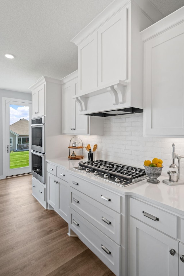 kitchen with appliances with stainless steel finishes, white cabinets, backsplash, and wood finished floors