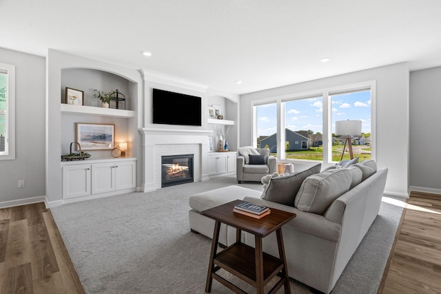 living room with built in features, a glass covered fireplace, baseboards, and wood finished floors