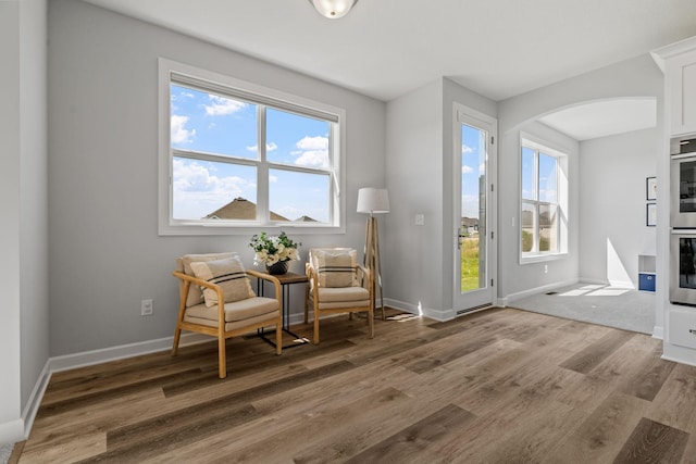 sitting room featuring arched walkways, baseboards, a healthy amount of sunlight, and light wood finished floors