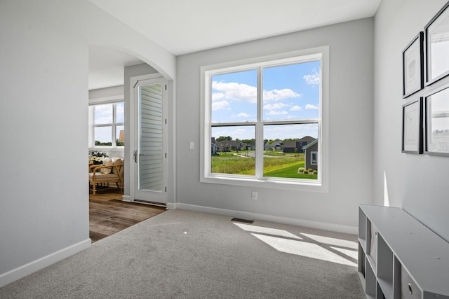 carpeted empty room with visible vents, baseboards, and arched walkways