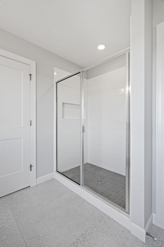 bathroom with a stall shower, a textured ceiling, and baseboards