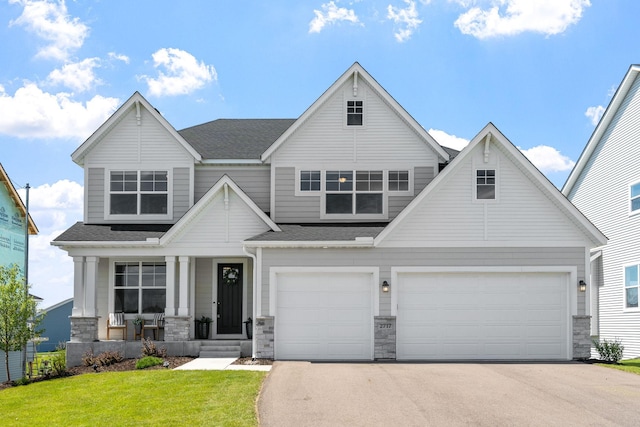 craftsman inspired home featuring concrete driveway, stone siding, roof with shingles, covered porch, and a front lawn