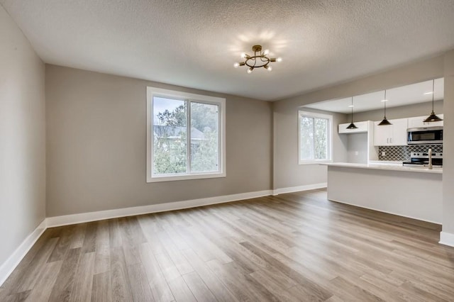 unfurnished living room with hardwood / wood-style flooring, a textured ceiling, and a notable chandelier