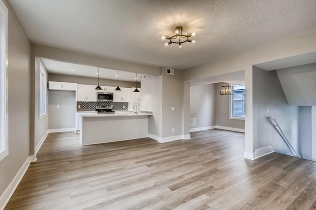 unfurnished living room featuring light wood-type flooring, a chandelier, a textured ceiling, and sink