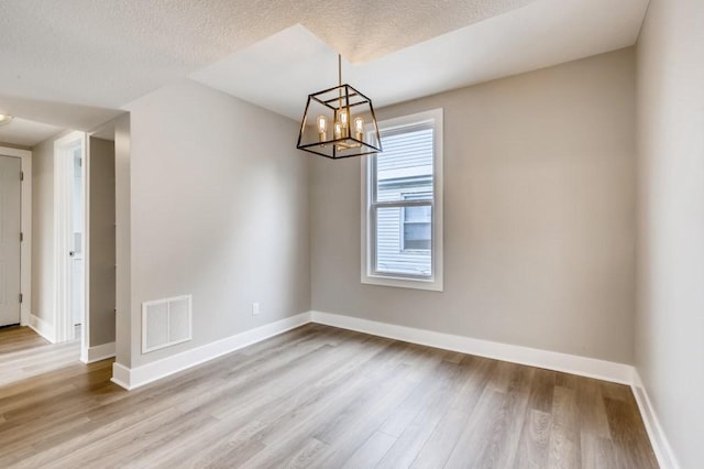 unfurnished room featuring a notable chandelier, light hardwood / wood-style flooring, and a textured ceiling