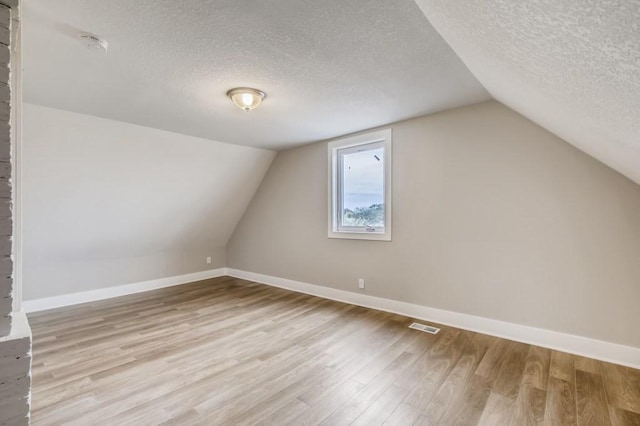 additional living space featuring a textured ceiling, lofted ceiling, and light wood-type flooring