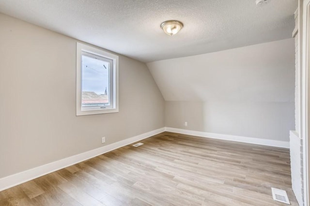 additional living space featuring vaulted ceiling, light hardwood / wood-style flooring, and a textured ceiling