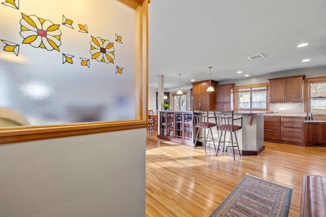 kitchen featuring visible vents, pendant lighting, brown cabinets, a kitchen breakfast bar, and light wood-style flooring