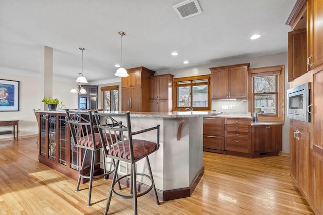 kitchen with visible vents, light wood-style floors, stainless steel microwave, a kitchen breakfast bar, and brown cabinets