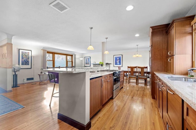 kitchen with visible vents, gas range, a breakfast bar, brown cabinetry, and a sink