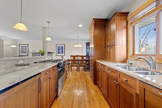 kitchen with stainless steel range with gas cooktop, decorative light fixtures, light wood-style flooring, brown cabinetry, and a sink