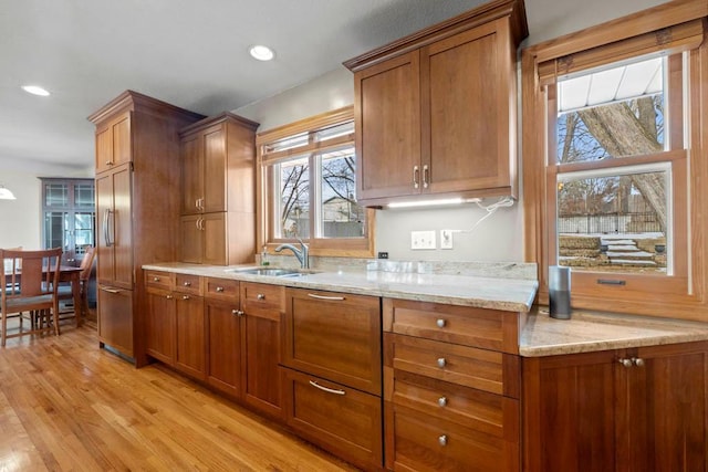 kitchen featuring light wood finished floors, brown cabinetry, built in fridge, and a sink