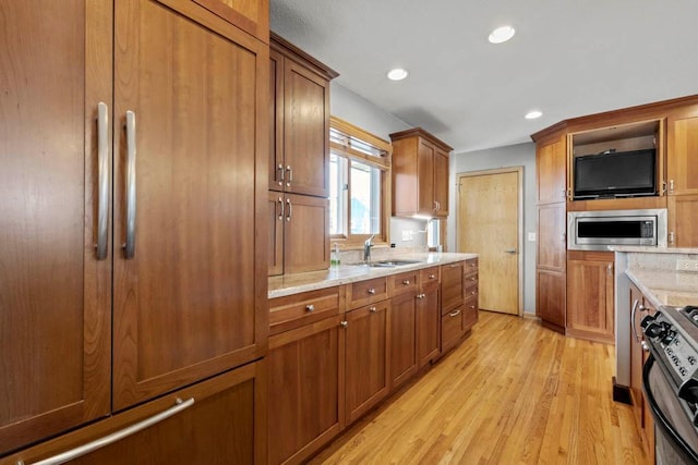 kitchen with brown cabinets, a sink, stainless steel microwave, range with gas stovetop, and light stone countertops