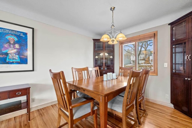 dining space with baseboards, light wood-type flooring, and an inviting chandelier