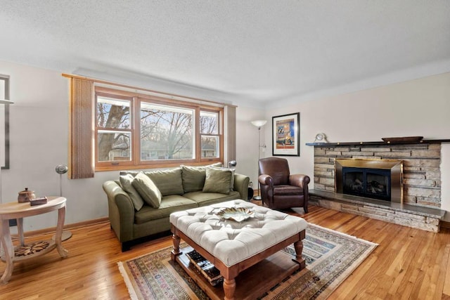 living area featuring baseboards, a textured ceiling, a stone fireplace, and wood finished floors