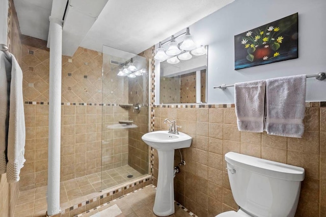 full bath featuring a wainscoted wall, a sink, a shower stall, tile walls, and toilet