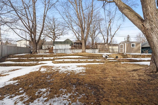 yard covered in snow featuring an outbuilding, a storage shed, and fence