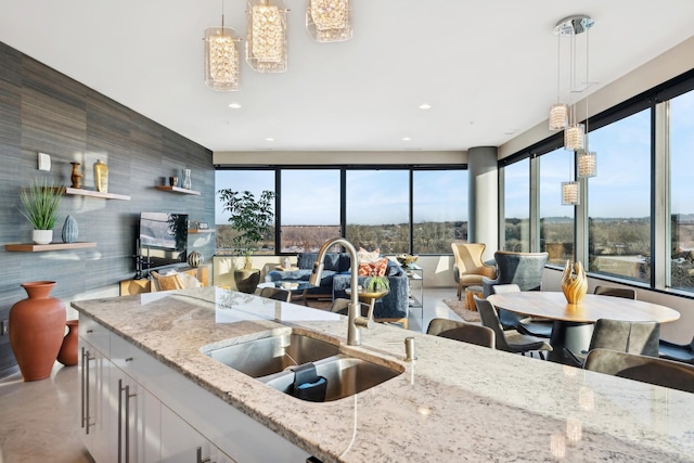 kitchen featuring light stone countertops, decorative light fixtures, white cabinets, and sink