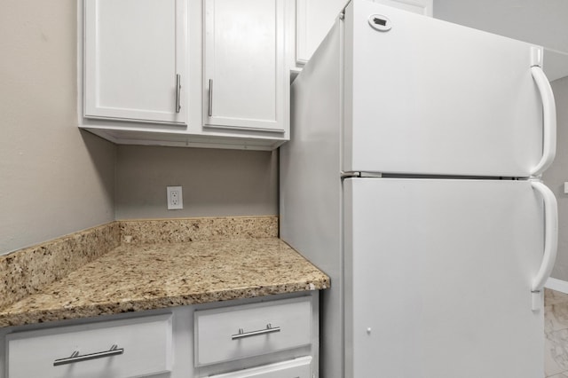 kitchen with white cabinetry, light stone countertops, and white fridge