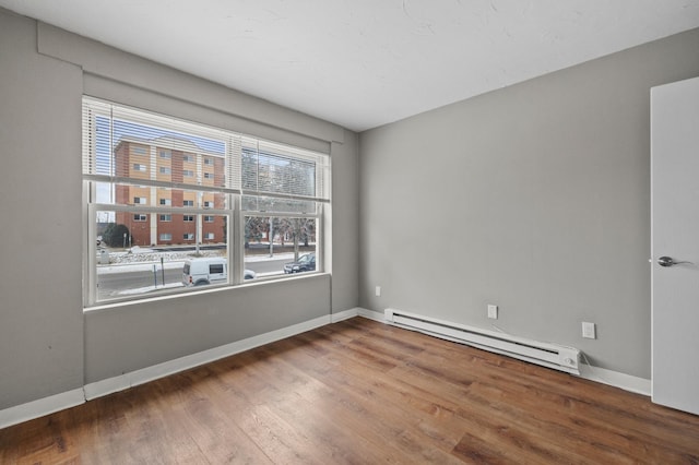 unfurnished room featuring a baseboard heating unit and wood-type flooring