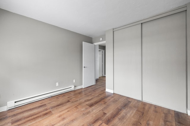 unfurnished bedroom with a baseboard radiator, hardwood / wood-style floors, and a closet