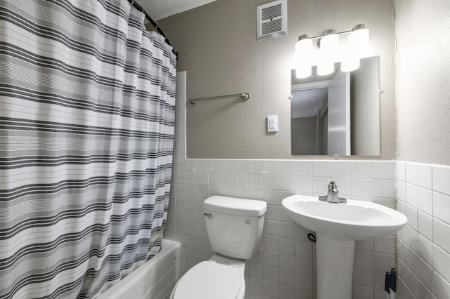 bathroom with tile walls, shower / tub combo, and toilet