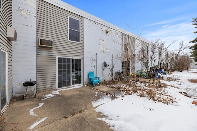 snow covered rear of property featuring a wall mounted air conditioner and a patio area