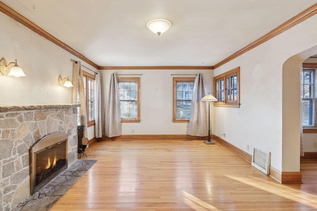 unfurnished living room featuring hardwood / wood-style floors, ornamental molding, and a stone fireplace