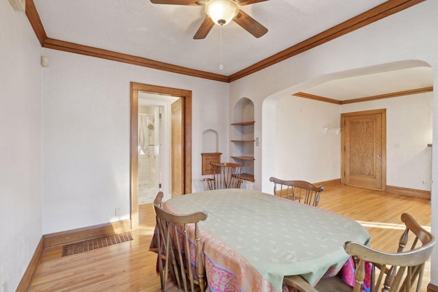 dining area featuring built in shelves, ceiling fan, crown molding, and light hardwood / wood-style floors