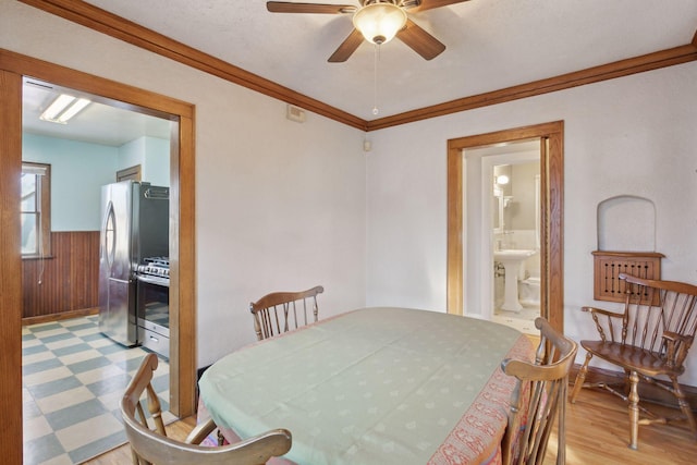 dining area with crown molding, light hardwood / wood-style floors, a textured ceiling, ceiling fan, and wood walls