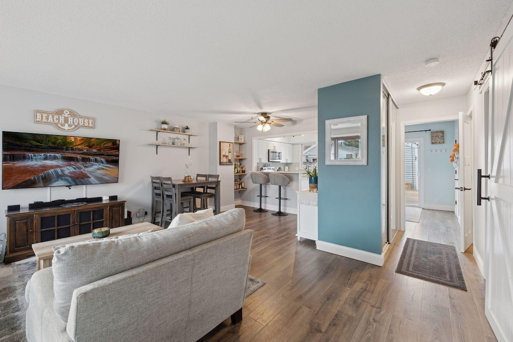 living room featuring a barn door, ceiling fan, dark hardwood / wood-style flooring, and a textured ceiling