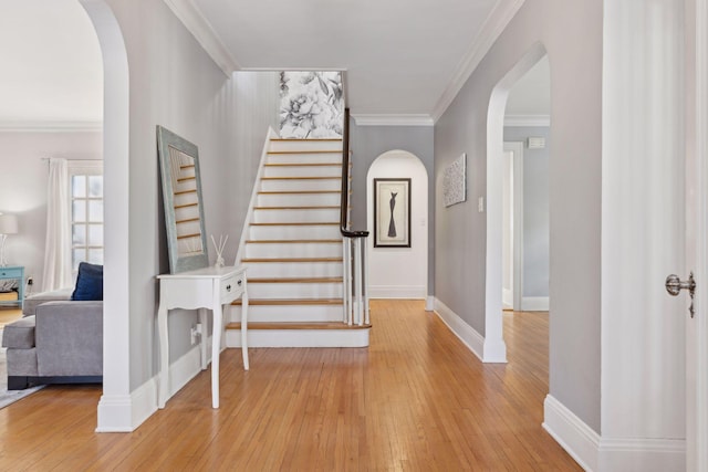 foyer entrance with light wood-type flooring, arched walkways, crown molding, and stairs