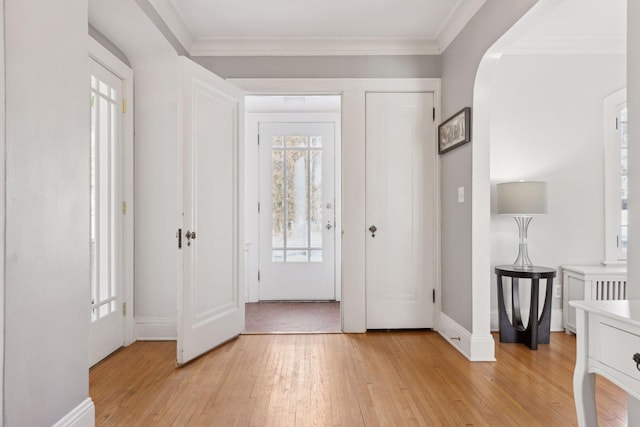 entryway featuring light wood-type flooring, baseboards, arched walkways, and crown molding