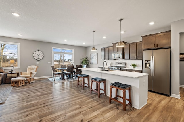 kitchen with stainless steel appliances, light hardwood / wood-style flooring, hanging light fixtures, and a center island with sink