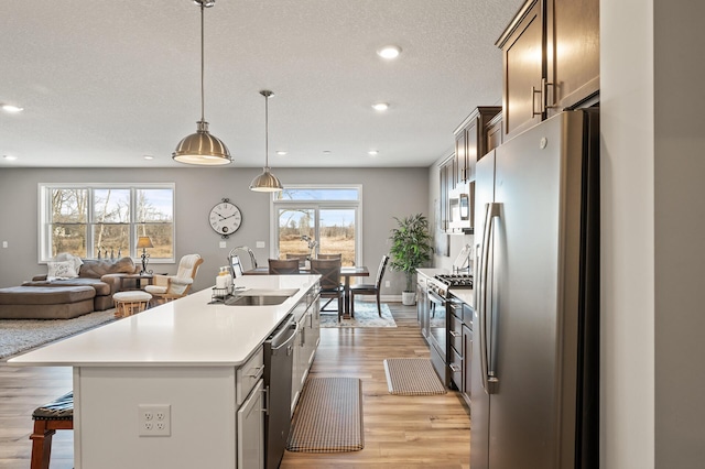 kitchen with sink, a kitchen island with sink, hanging light fixtures, stainless steel appliances, and light hardwood / wood-style floors