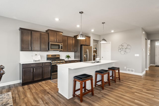 kitchen with a breakfast bar area, appliances with stainless steel finishes, dark brown cabinets, a center island with sink, and decorative light fixtures