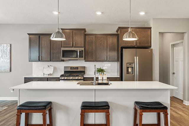 kitchen with pendant lighting, stainless steel appliances, an island with sink, and tasteful backsplash