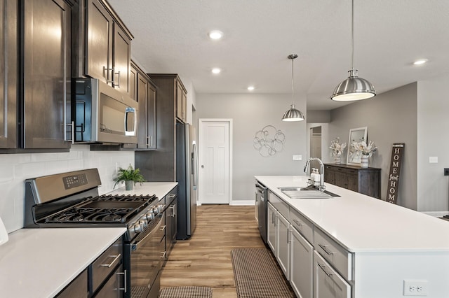 kitchen featuring appliances with stainless steel finishes, sink, backsplash, hanging light fixtures, and a kitchen island with sink