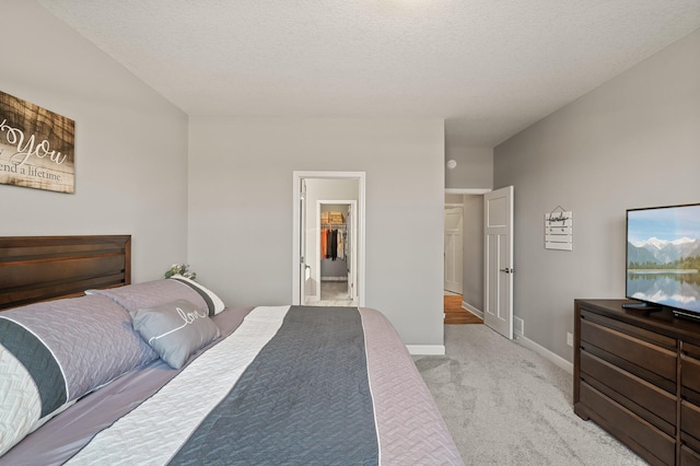 bedroom featuring a walk in closet, light carpet, a textured ceiling, and a closet