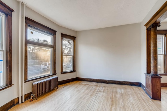 empty room with light hardwood / wood-style floors, radiator, and ornate columns