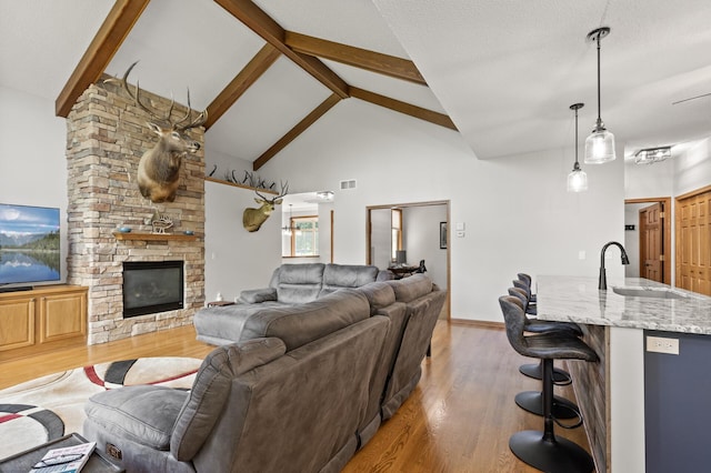 living room featuring beamed ceiling, a fireplace, sink, high vaulted ceiling, and light hardwood / wood-style flooring