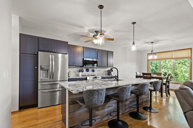 kitchen with hanging light fixtures, appliances with stainless steel finishes, a center island with sink, and a breakfast bar area