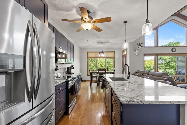 kitchen featuring hanging light fixtures, sink, a textured ceiling, a center island with sink, and stainless steel appliances