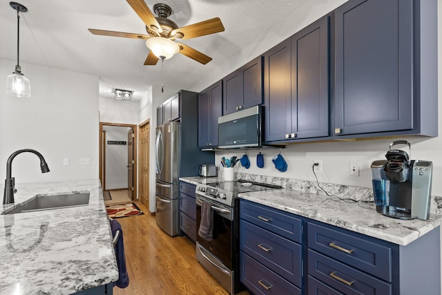 kitchen with a textured ceiling, stainless steel appliances, sink, blue cabinetry, and light hardwood / wood-style flooring